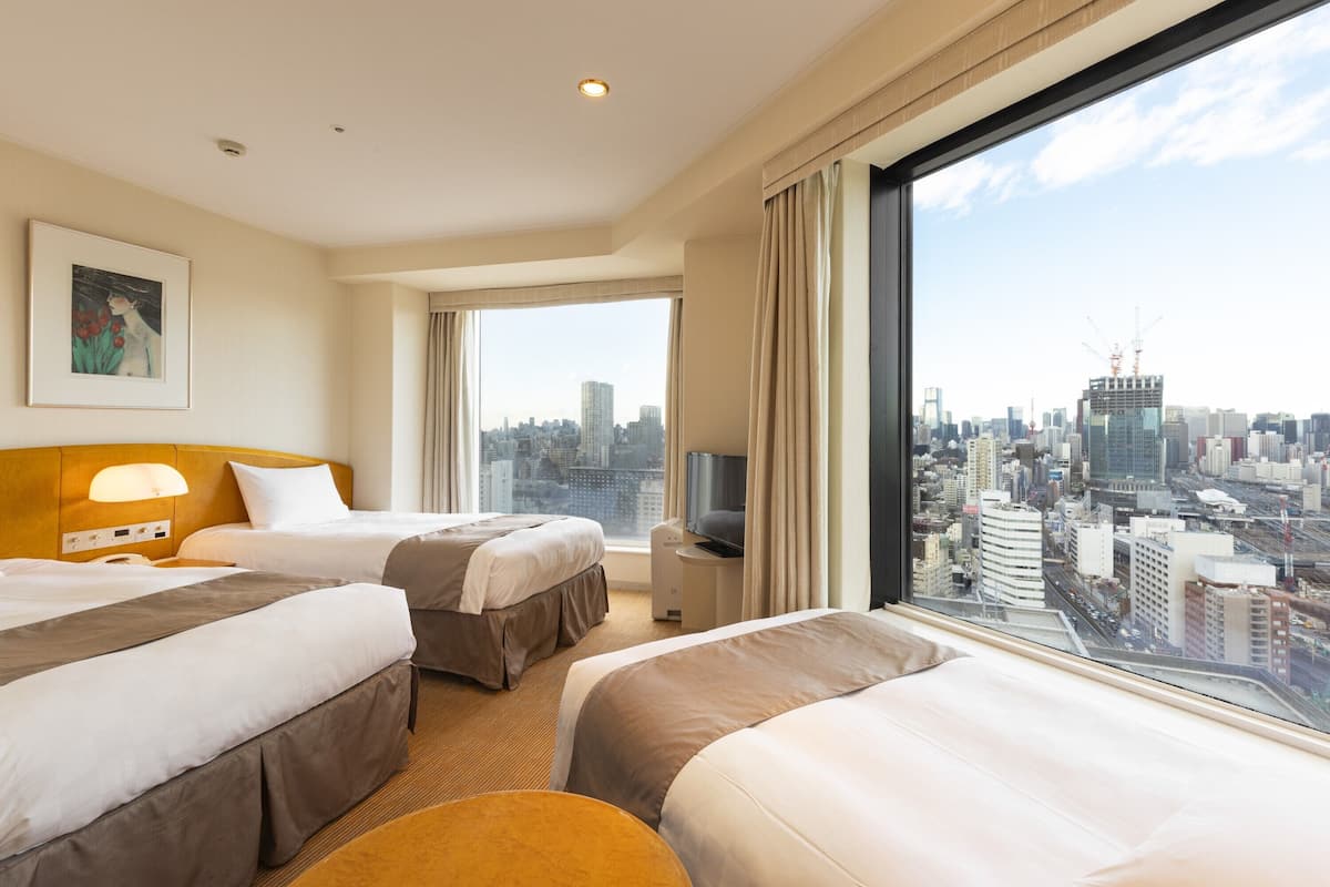 A hotel room with two beds, a television, and a large window with a city view.
