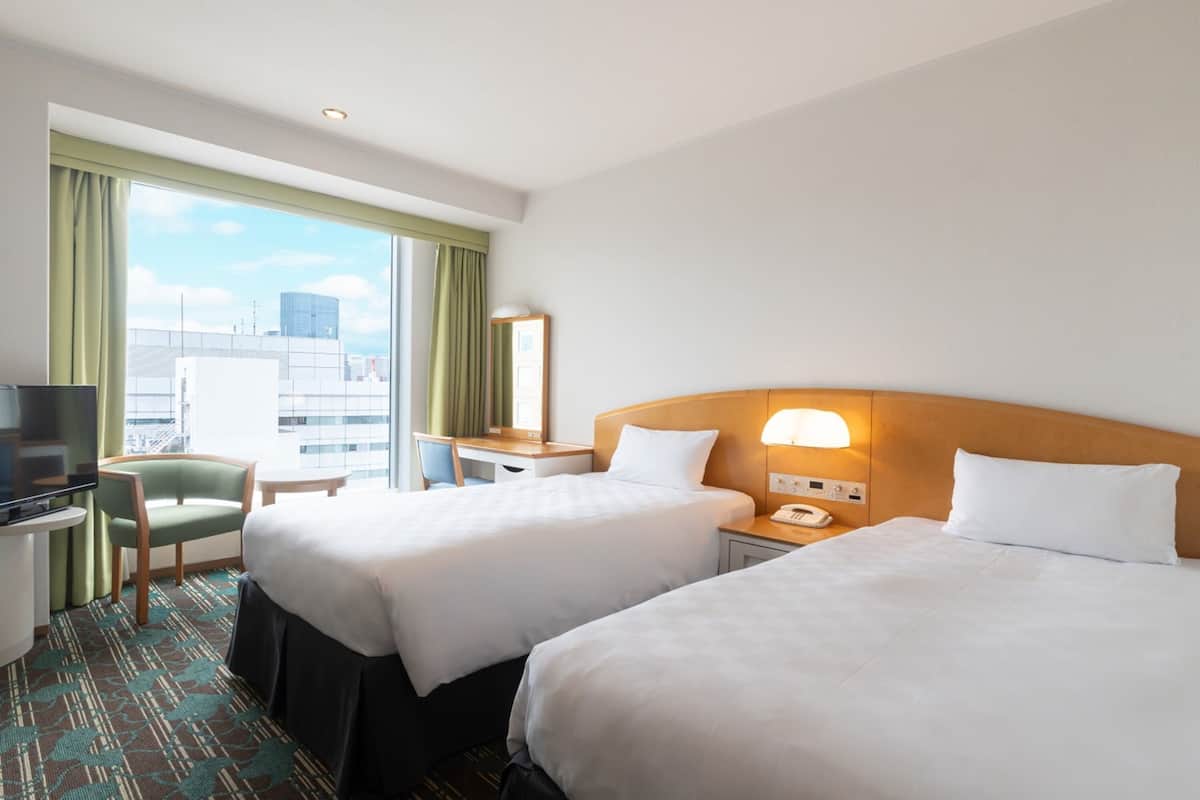 A hotel room with two beds, a desk, a chair, a TV, and a city view.