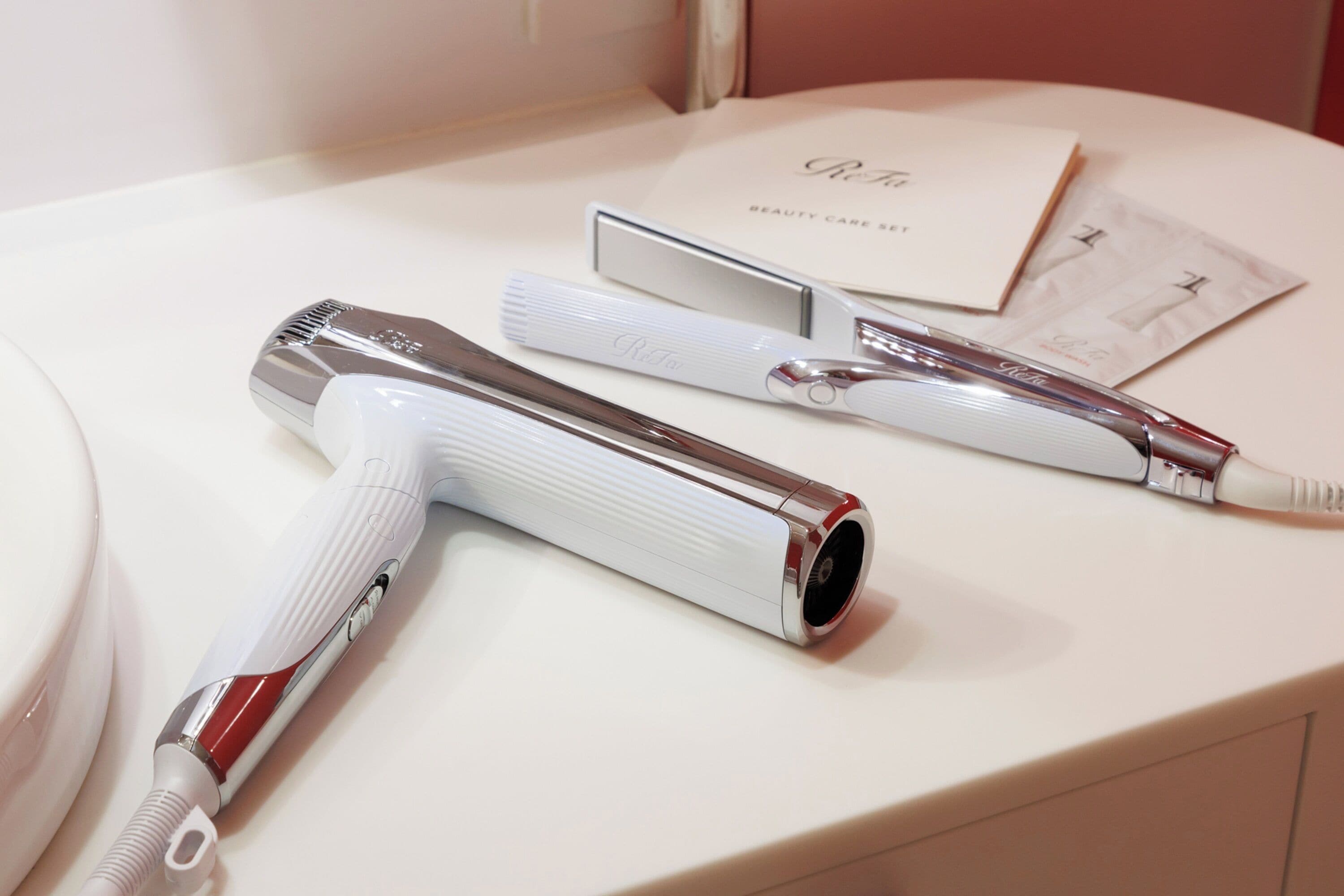 A bathroom with a white countertop, a mirror, and a set of grooming tools including a hairdryer, a comb, and a razor.