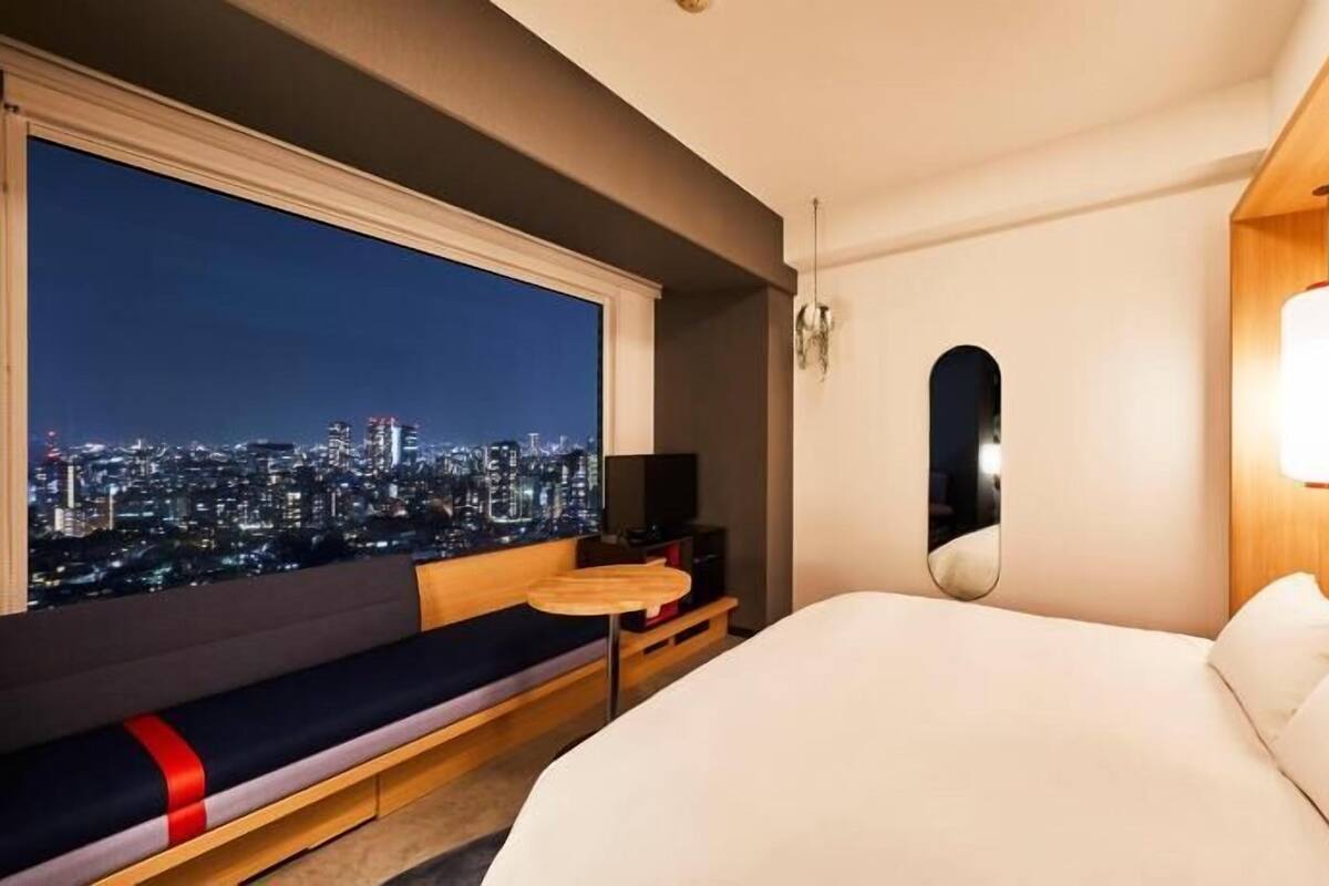 A hotel room with a city view, a bed, a bedside table, a TV, and a seating area with a view.