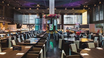 A spacious restaurant with multiple dining tables and chairs, a central decorative column, and large windows providing natural light.