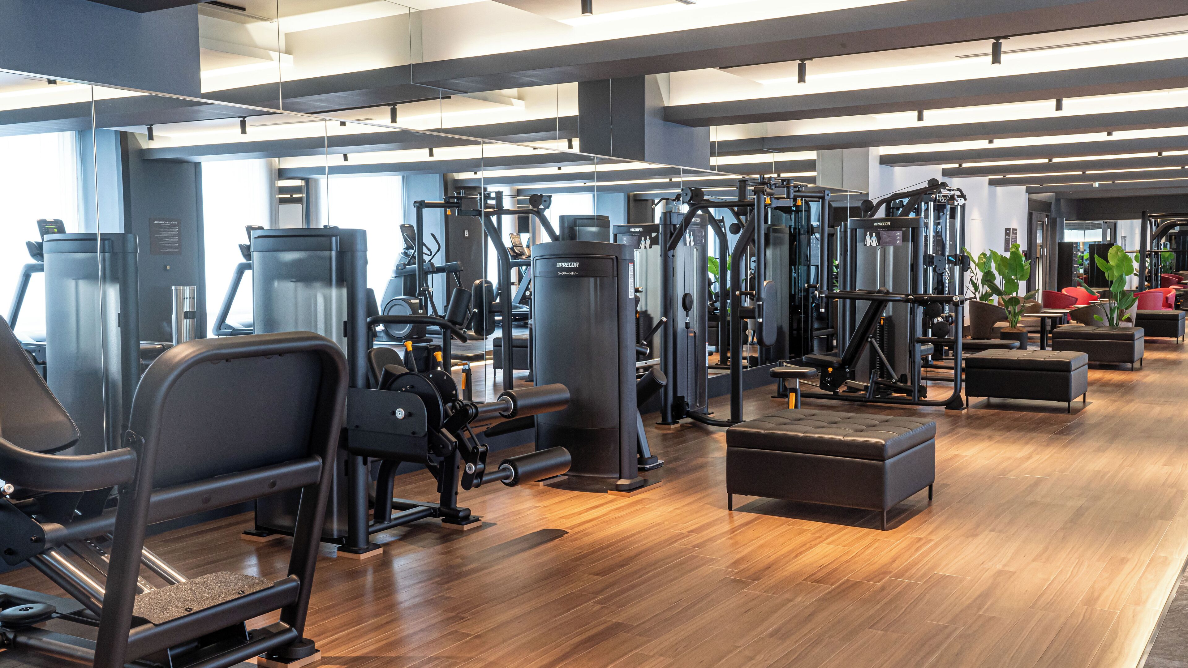 Une salle de sport moderne équipée de divers appareils d’exercice, dotée d’un plancher en bois et d’espaces aménagés pour se détendre.