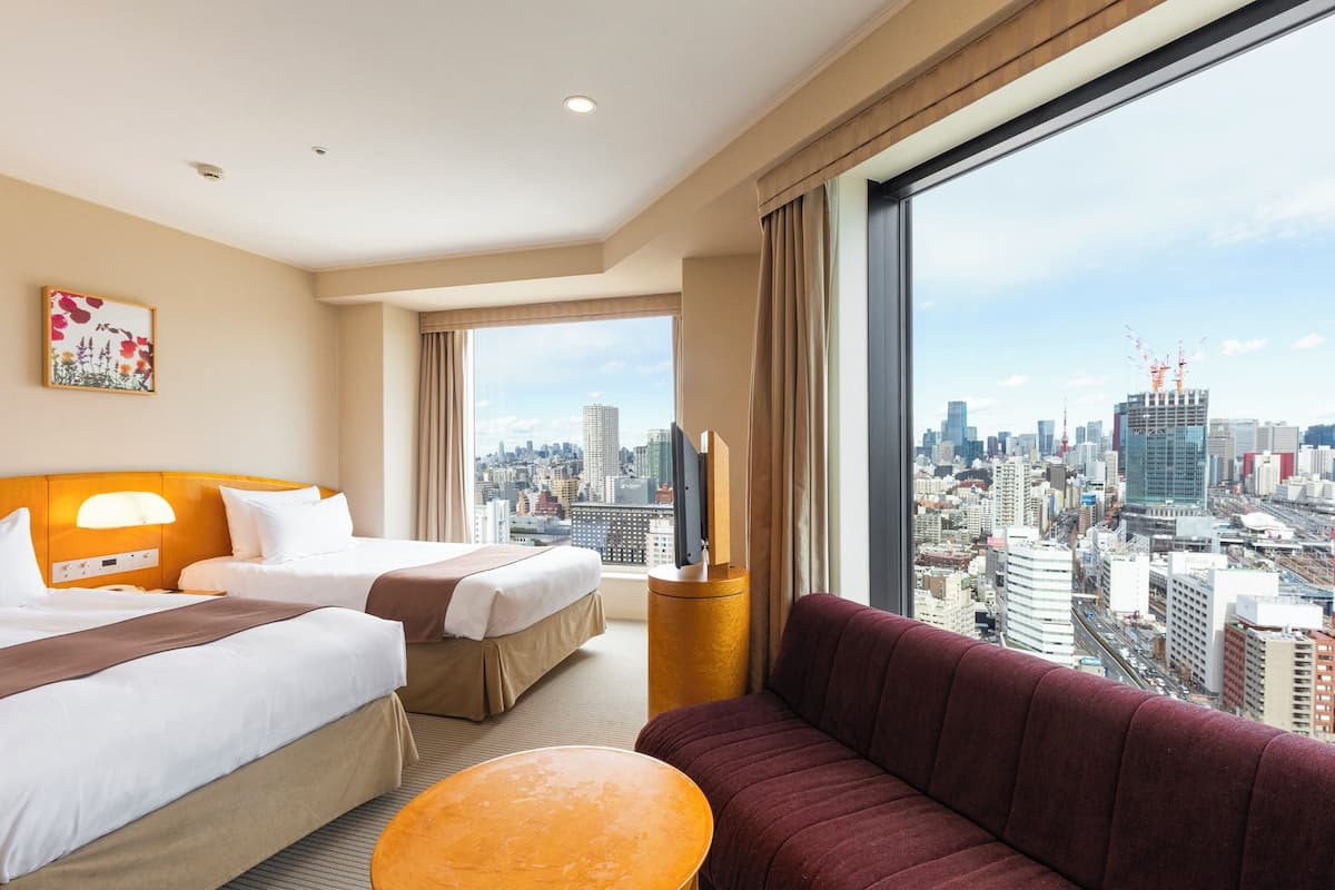 A hotel room with two beds, a sofa, a television, and a large window with a city view.
