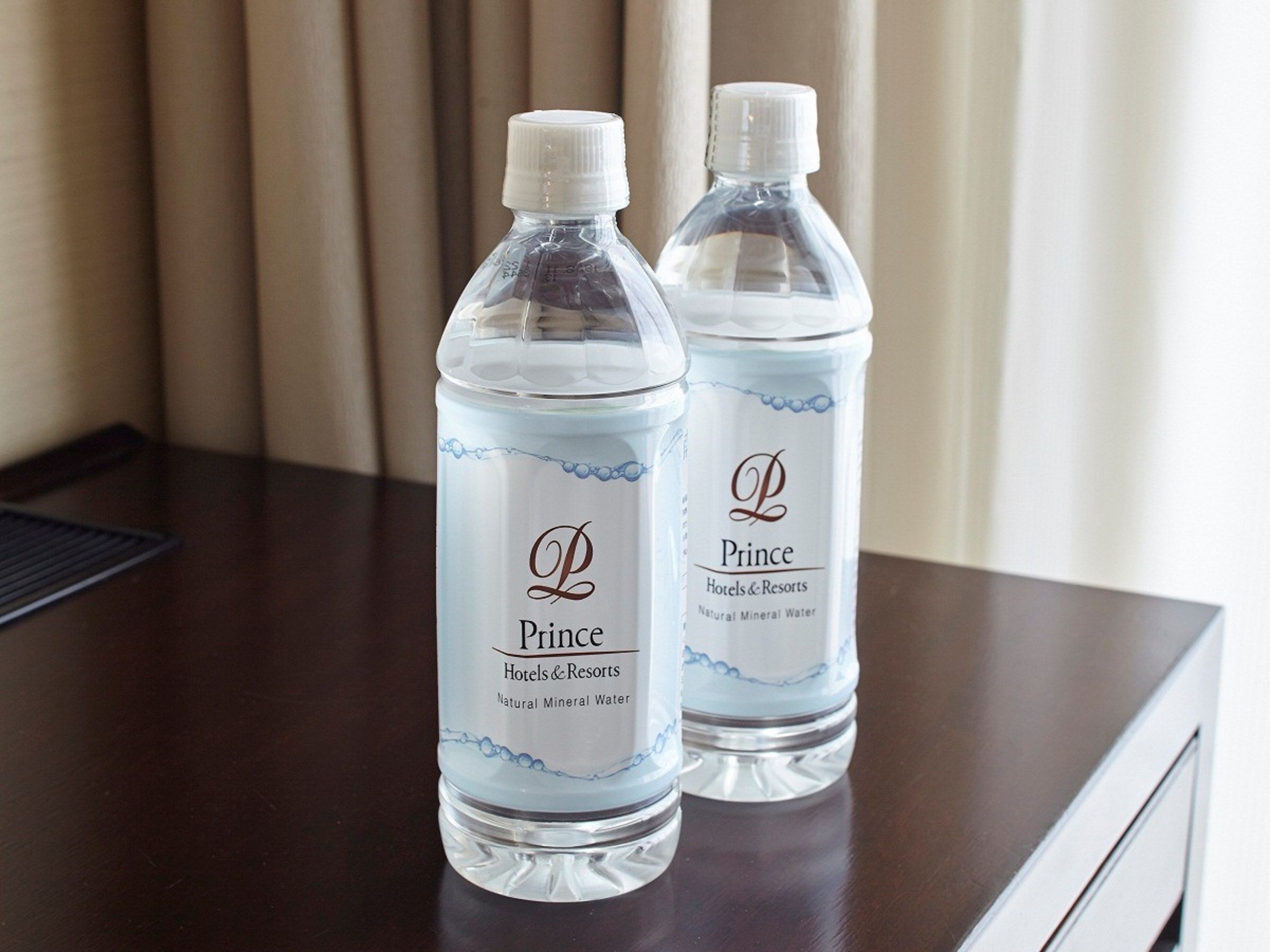 Two bottles of water labeled 'Prince Hotels & Resorts' on a wooden table.