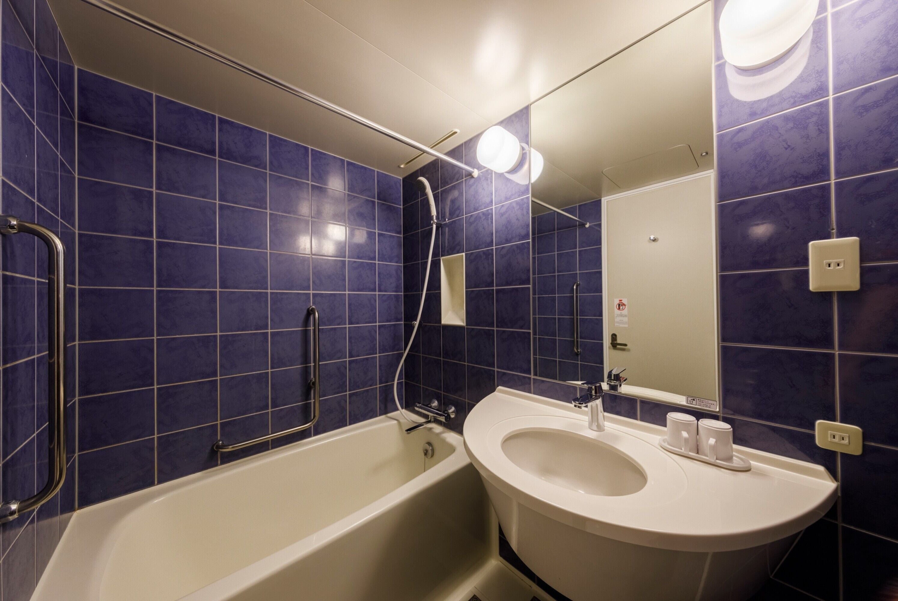 A bathroom with blue tiles, a white bathtub, and a sink with a mirror above it.