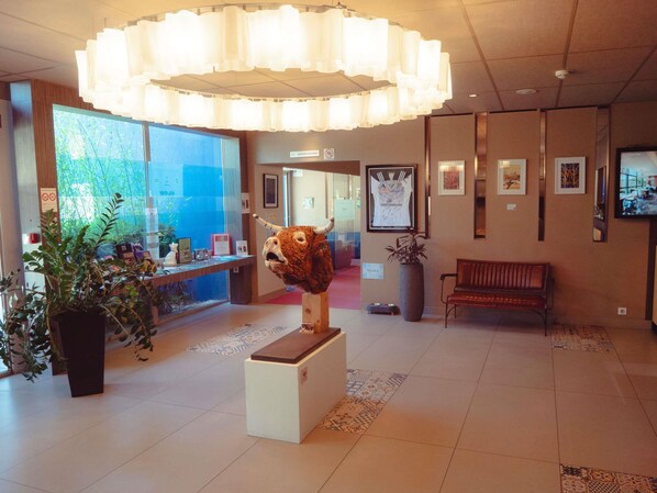 A lobby with a reception desk, a large sculpture, a bench, and framed artwork on the walls.
