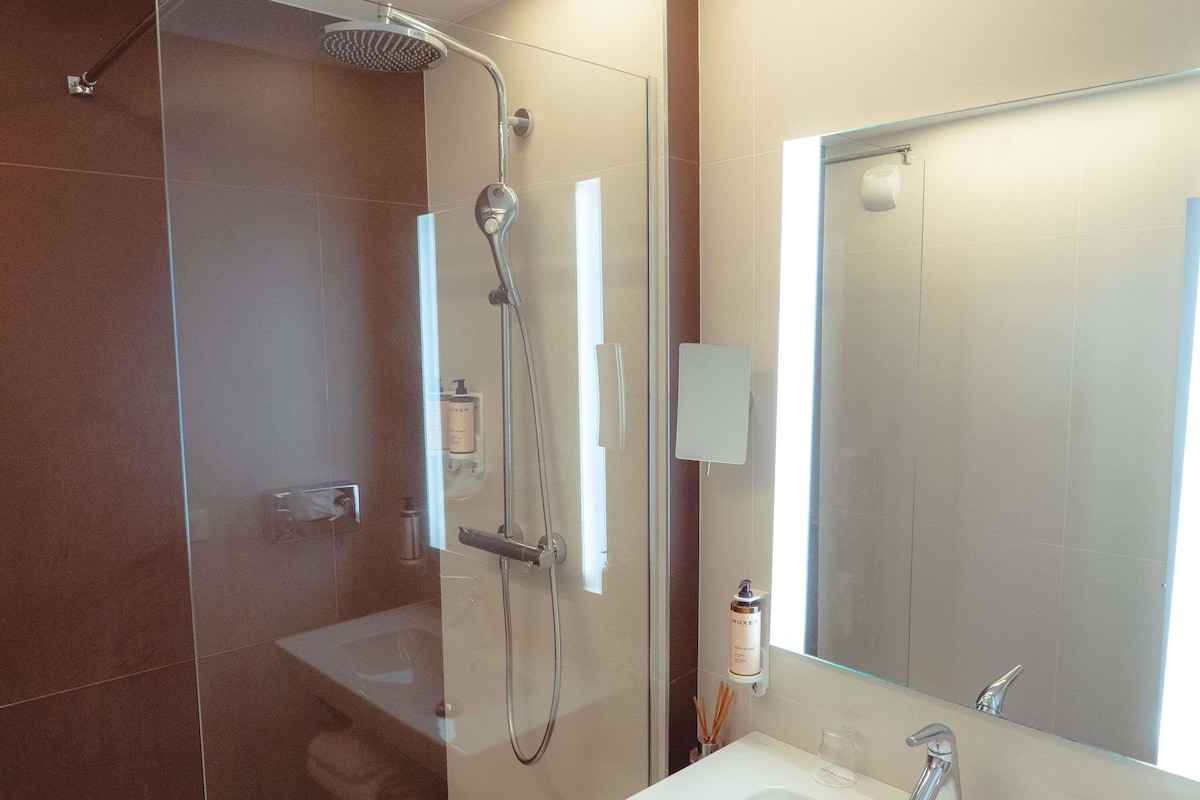 Un baño moderno con cabina de ducha de vidrio, un lavabo blanco y un espejo grande.