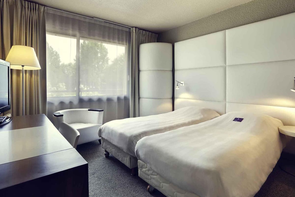 Habitación de hotel con dos camas, un escritorio, una silla y un televisor.
