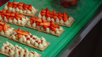 Une planche à découper verte sur laquelle sont disposés plusieurs petits gâteaux carrés, garnis de fraises et de crème.