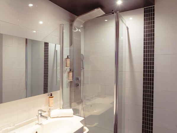 A modern bathroom with a glass shower enclosure, a white sink, and a large mirror.