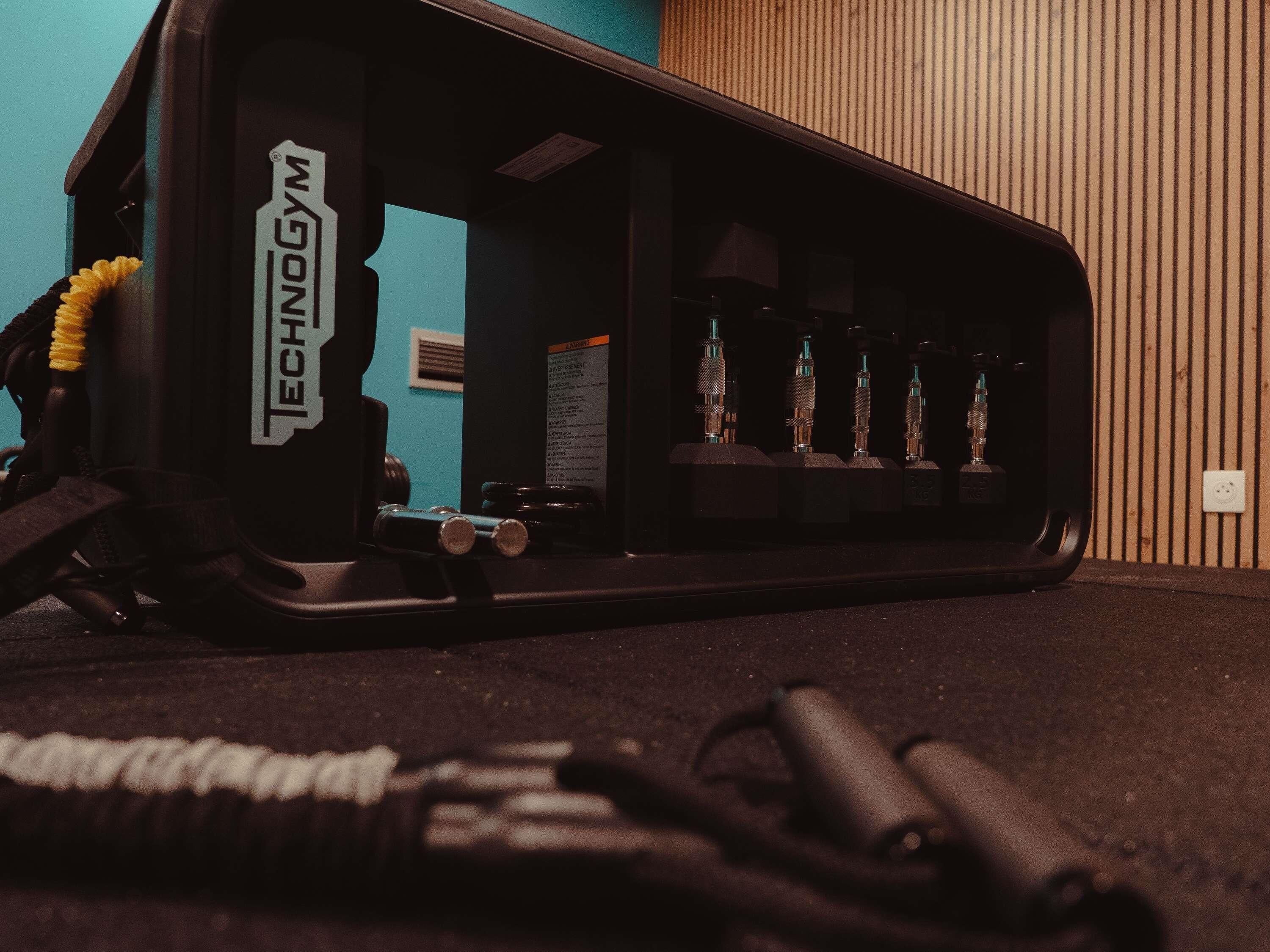 Un gimnasio con equipo de ejercicio, un estante con botellas en la pared y una pared azul de fondo.