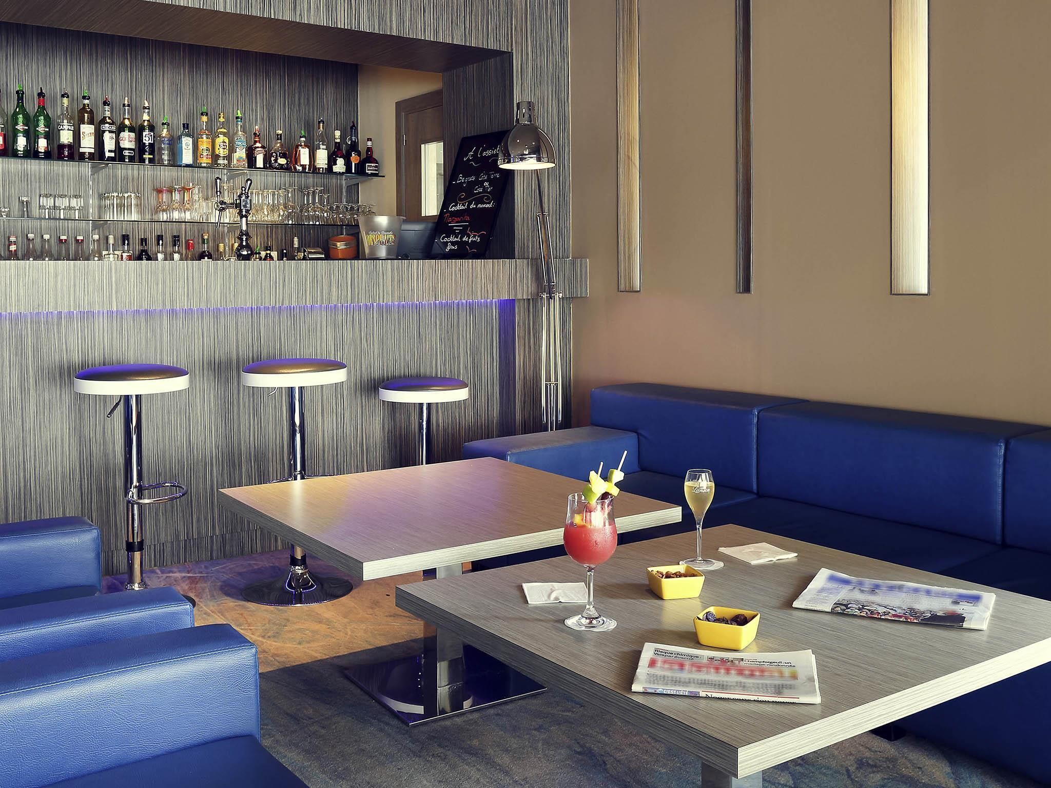 A bar area with a variety of liquor bottles, a chalkboard menu, and a seating area with a table and chairs.