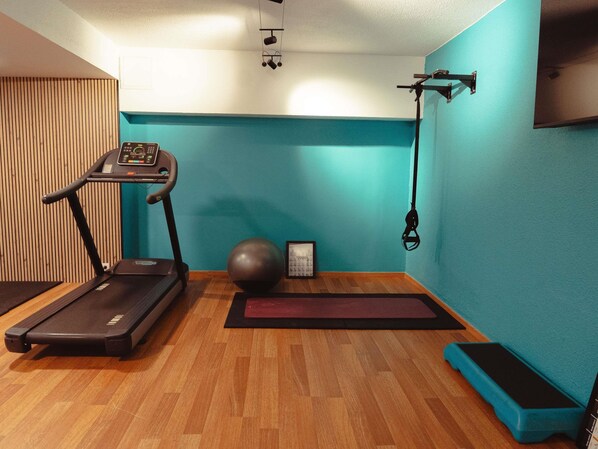 Una habitación con una cinta de correr, una bicicleta estática, una pelota medicinal, una colchoneta para yoga y una barra de dominadas.