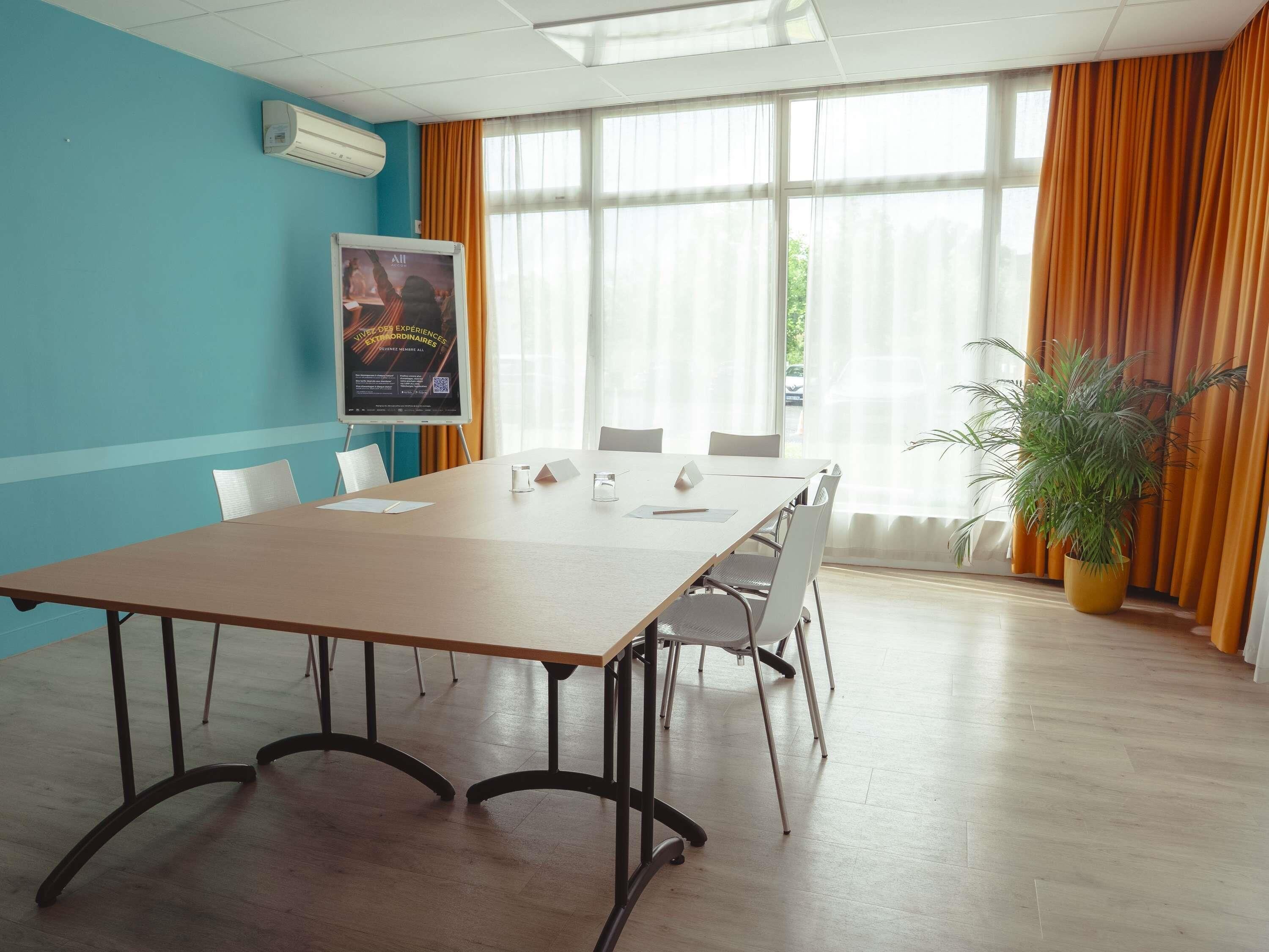 A conference room with a long table, chairs, a poster on the wall, and a potted plant.
