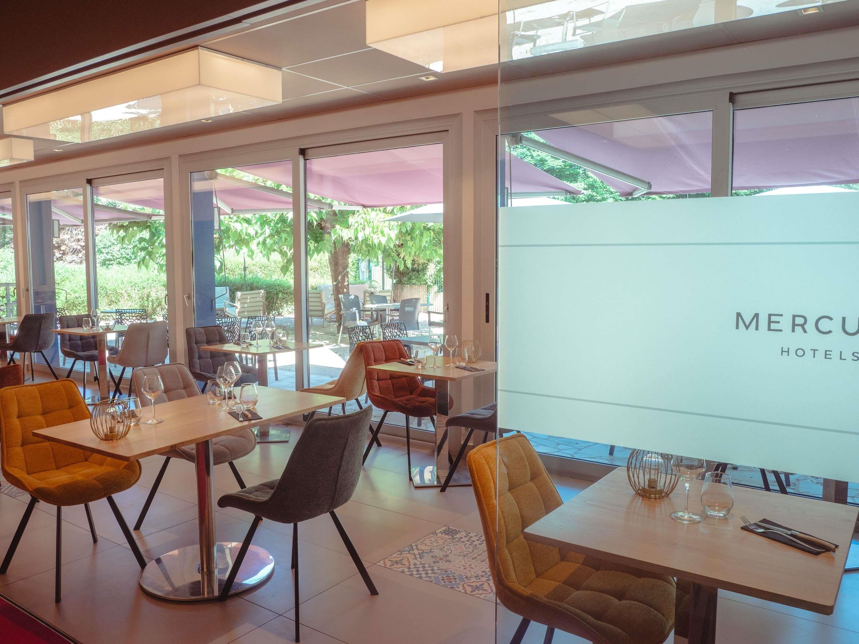 Un espace de restauration intérieur moderne, doté de tables et de chaises, de grandes fenêtres et offrant une vue sur l’extérieur.