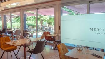 Un espace de restauration intérieur moderne, doté de tables et de chaises, de grandes fenêtres et offrant une vue sur l’extérieur.