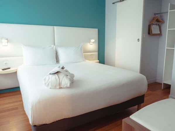 A neatly made bed with white linens, a headboard, bedside tables with lamps, and a wooden floor.