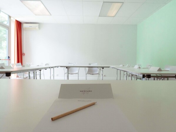 A conference room with a long table, chairs, a whiteboard, and a window with curtains.
