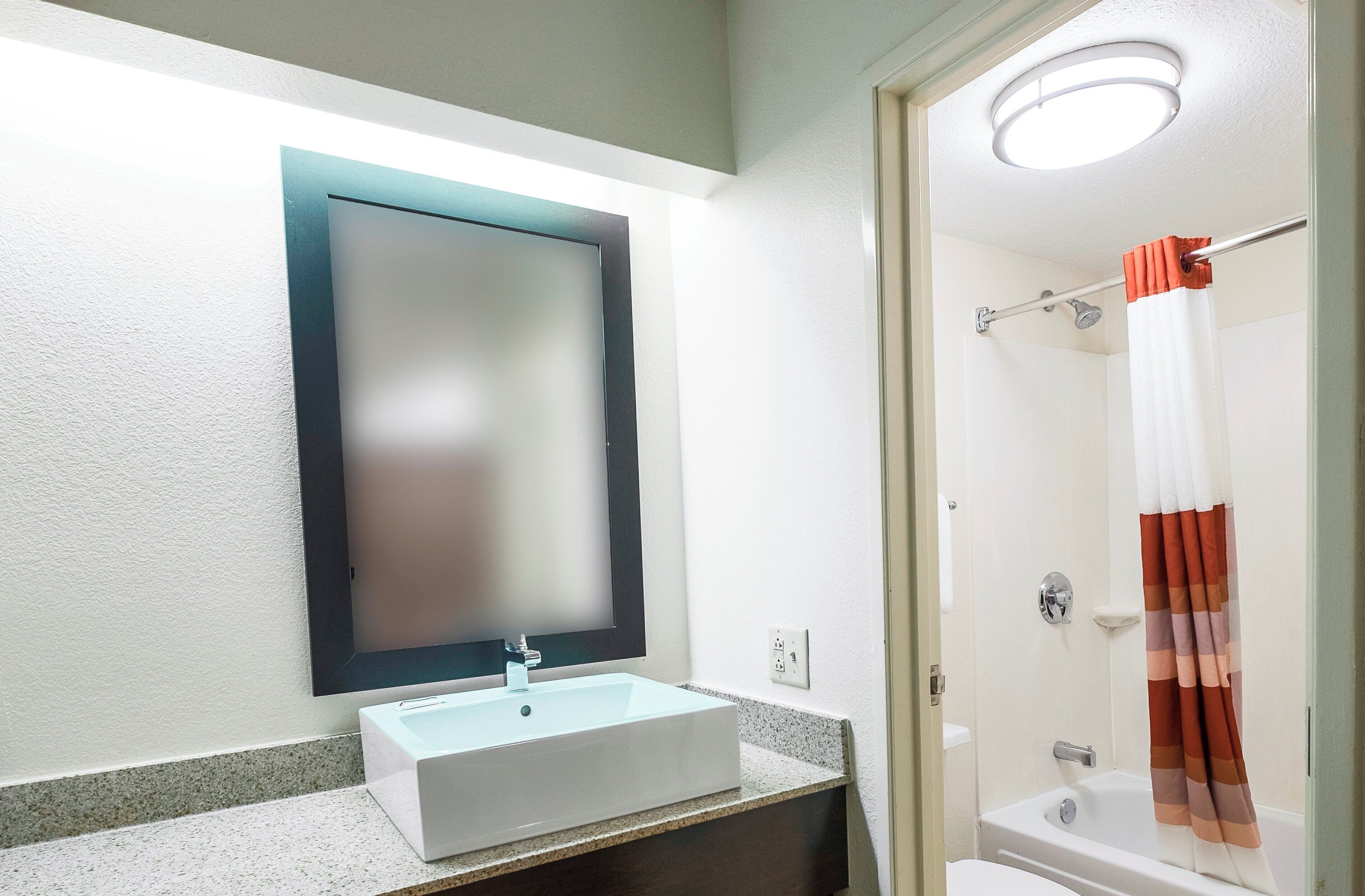 A bathroom with a white sink, a mirror, a shower with a curtain, and a toilet.