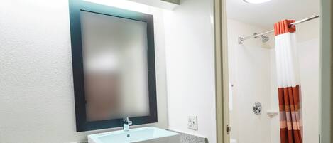 A bathroom with a white sink, a mirror, a shower with a curtain, and a toilet.