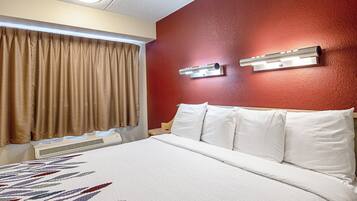 Une chambre d’hôtel équipée d’un lit, de rideaux, d’un climatiseur fixé au mur et d’un luminaire.