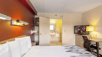 A hotel room with a bed, a desk, a chair, a television, and a bathroom visible through an open door.
