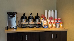 Una estación de café con varias máquinas de café, vasos desechables y dispensadores de crema para café.
