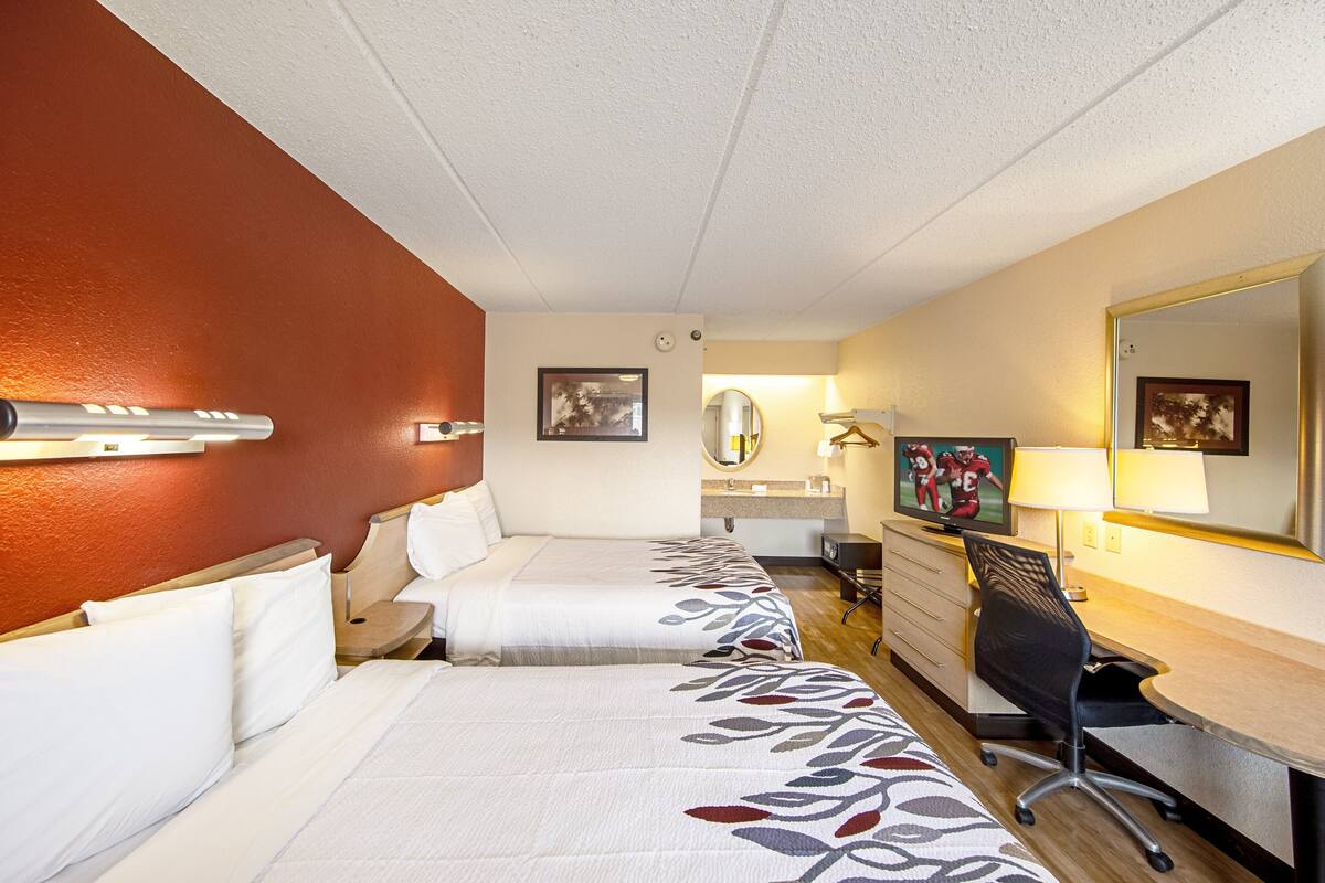 A hotel room with two beds, a desk, a chair, a TV, and a mirror.