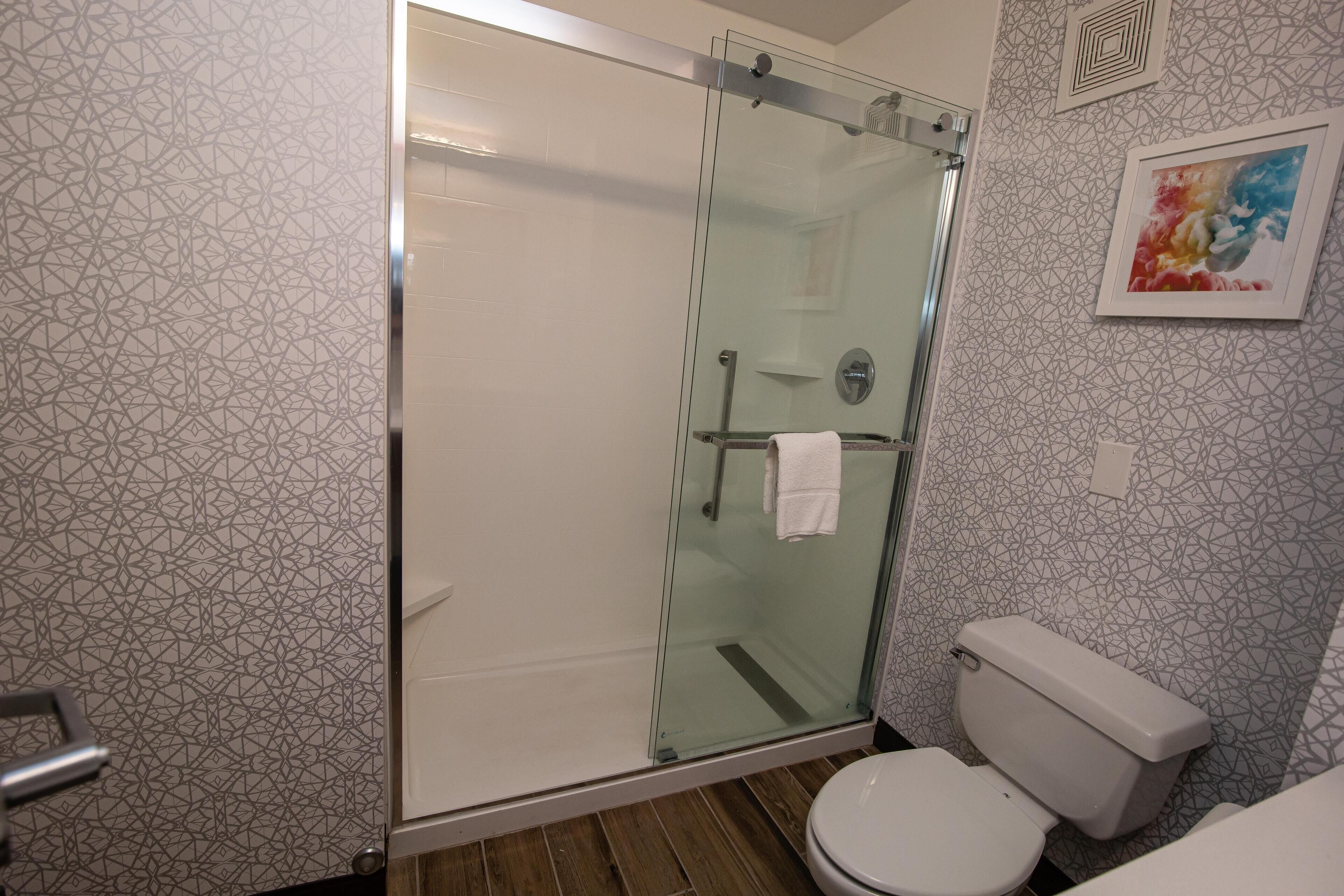 A bathroom with a glass-enclosed shower, a toilet, and patterned walls.