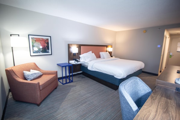 A hotel room with a bed, a desk, a chair, a lamp, and a painting on the wall.