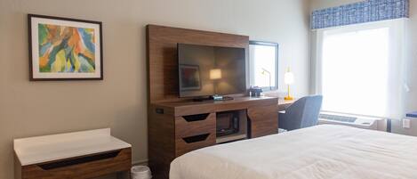 Quarto de hotel com cama, televisão, secretária e cadeira.
