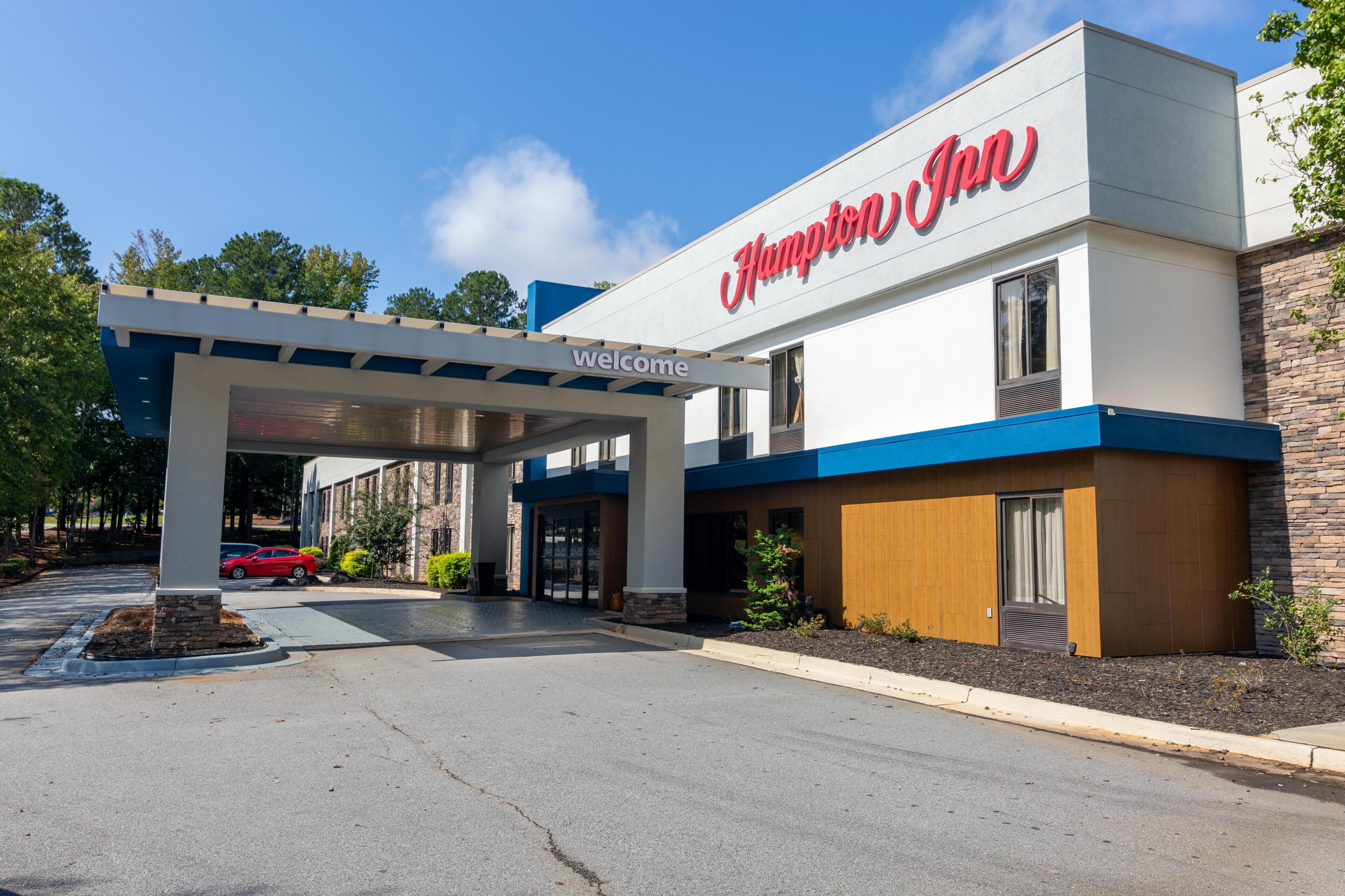 A Hampton Inn with a 'Welcome' sign, a covered parking area, and a brick facade.
