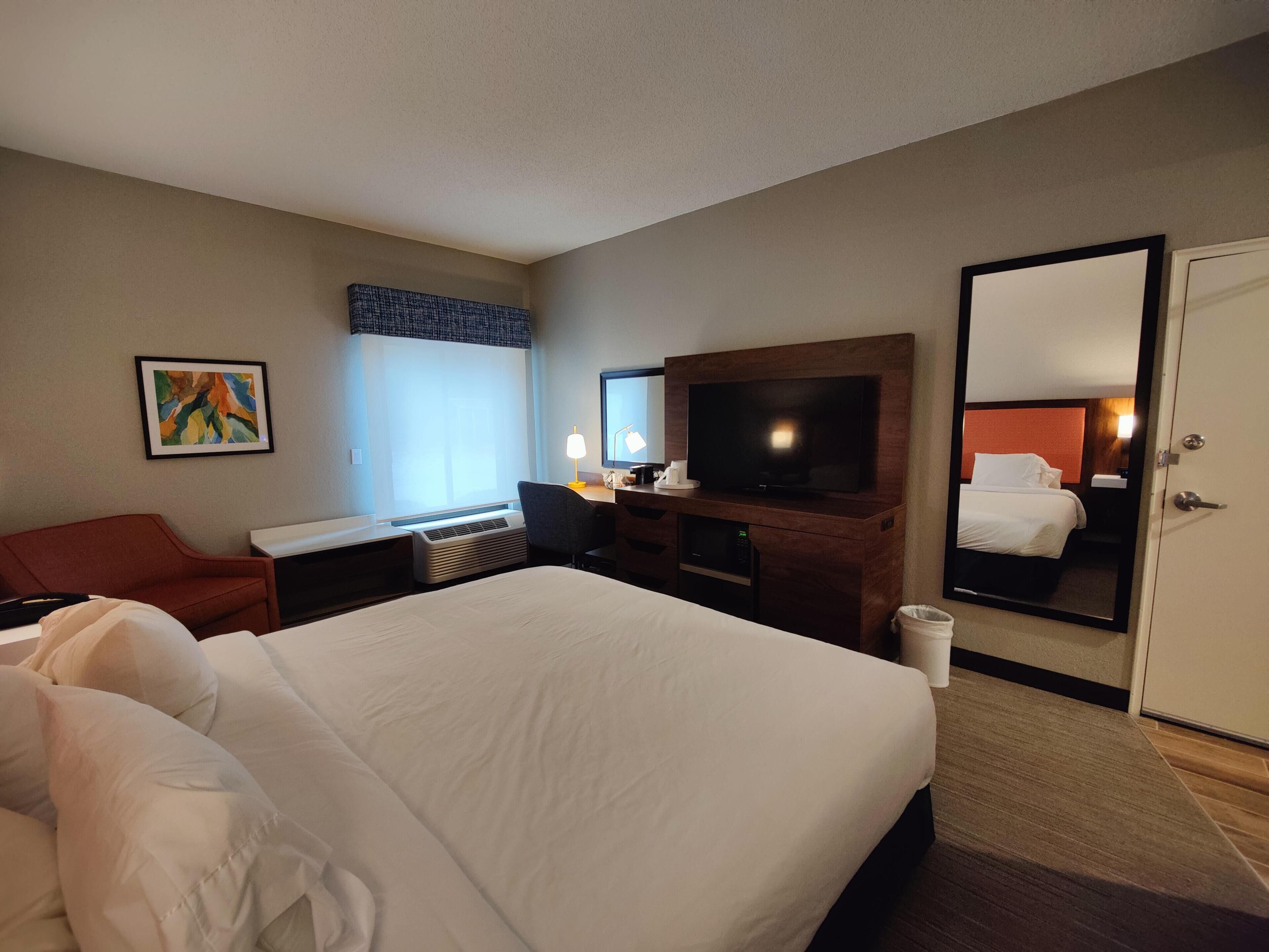 A hotel room with a bed, desk, chair, TV, and a mirror.