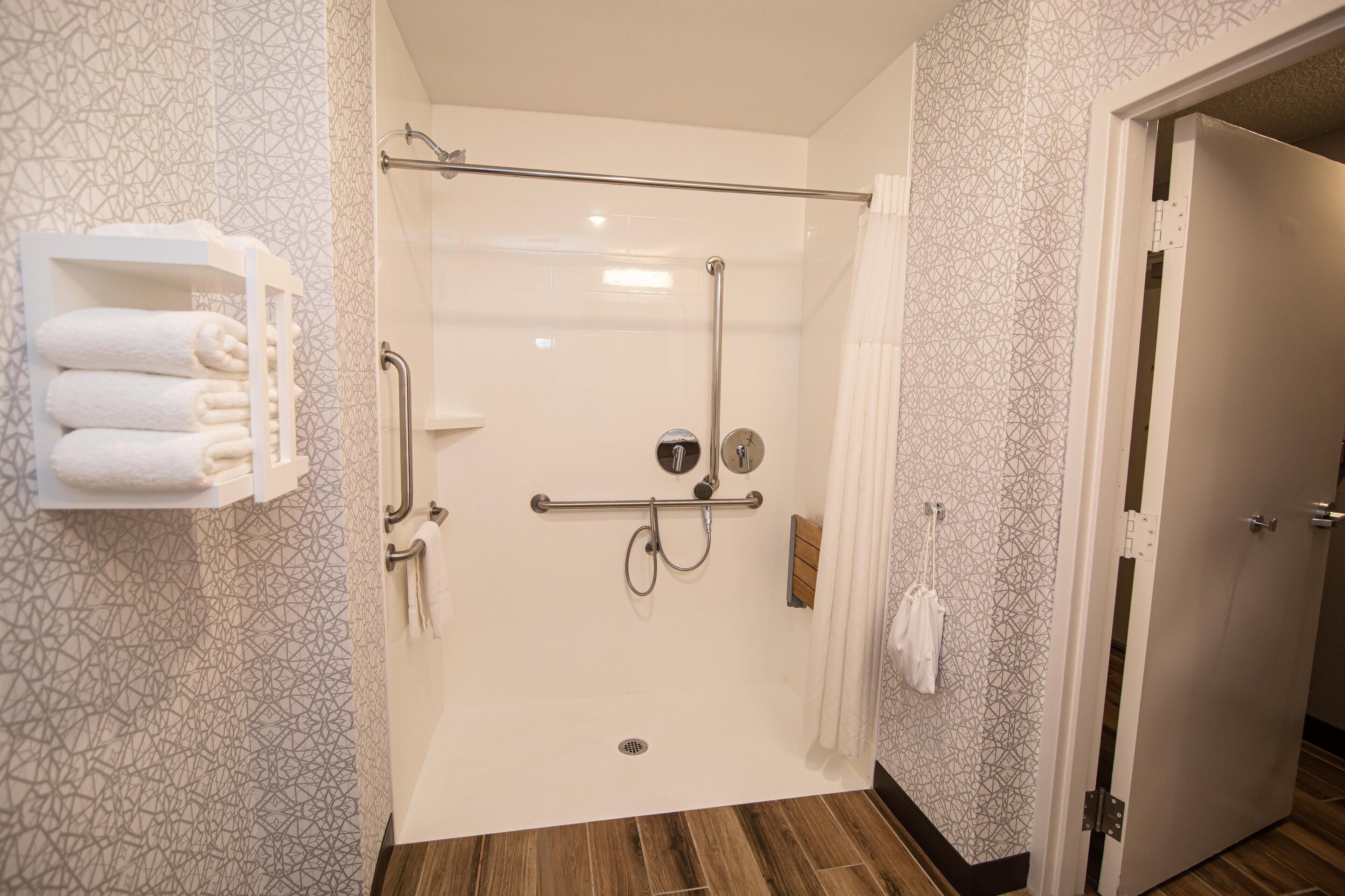 A shower with a glass door, a towel rack with folded towels, and a wooden floor.