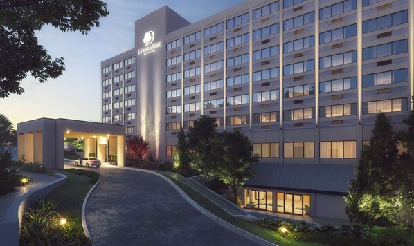 Un hôtel moderne, avec une enseigne bien visible, une entrée abritée et une allée bordée de verdure.