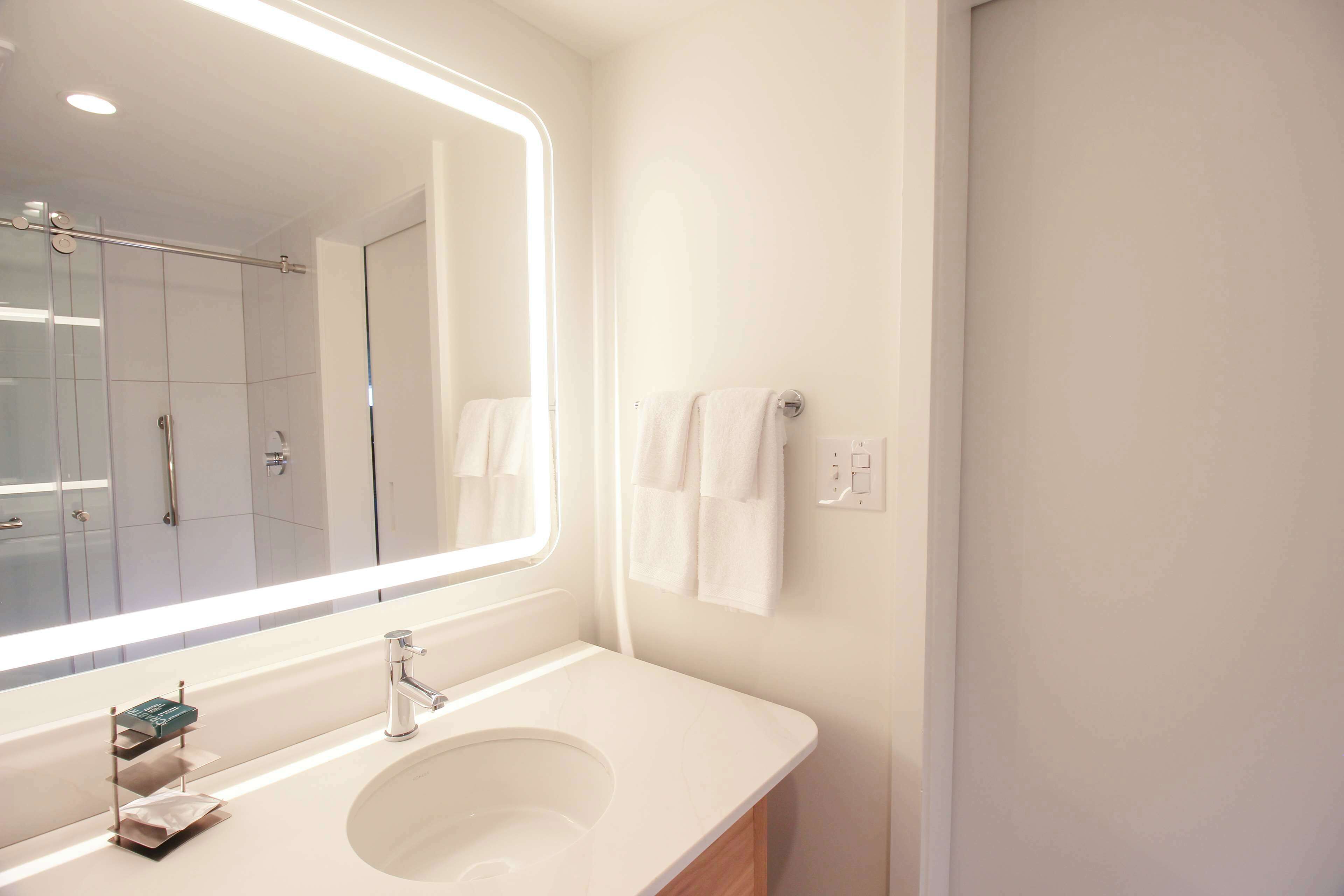 A modern bathroom with a large mirror, a white sink, and a glass shower enclosure.