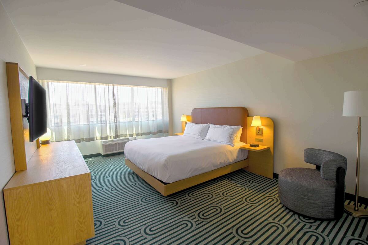 Une chambre d’hôtel avec un lit, un bureau, une chaise, une télévision et une fenêtre avec des rideaux.