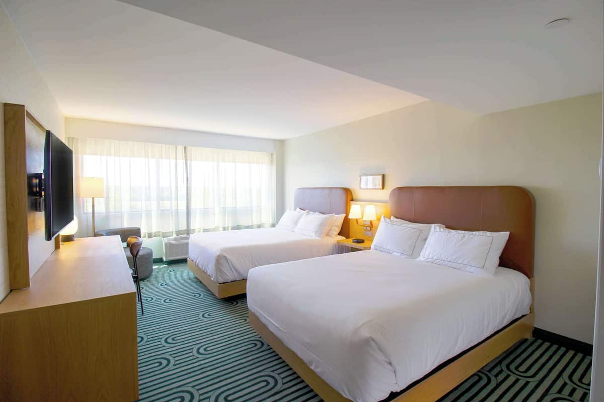 Une chambre d’hôtel avec deux lits, un bureau, une télévision et une fenêtre avec des rideaux.