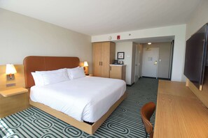 Une chambre d’hôtel avec un grand lit, des tables de chevet avec des lampes, un bureau en bois, une chaise, une télévision et un coin cuisine.