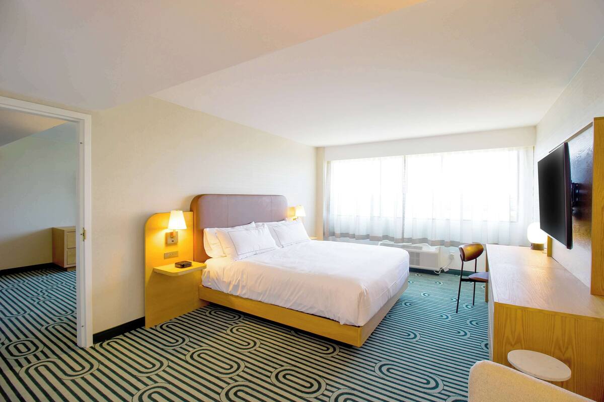 Une chambre d’hôtel comprenant un lit, des tables de chevet, un bureau, une chaise, une télévision et une fenêtre avec des rideaux.