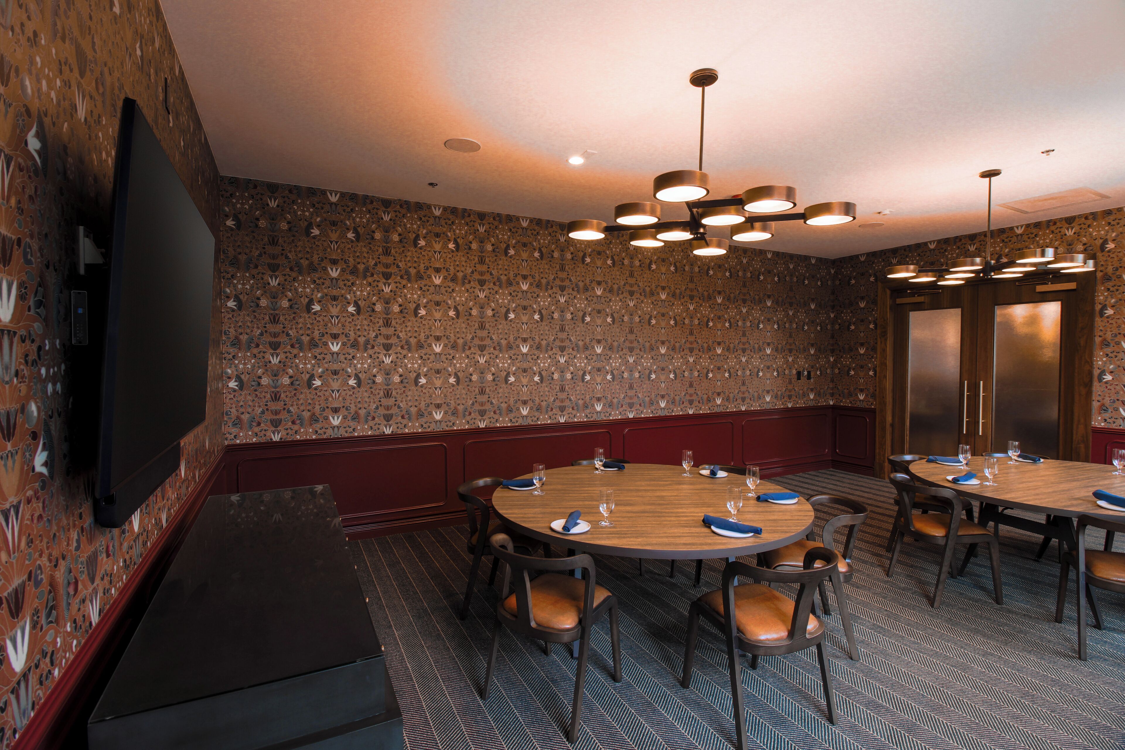 Une salle de conférence équipée d’une grande table, de chaises, d’un téléviseur à écran plat et d’un mur orné d’un motif décoratif.