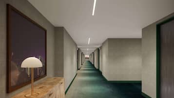 Un pasillo largo y estrecho con alfombra verde, un banco de madera con una lámpara y obras de arte enmarcadas en las paredes.