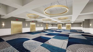 Une salle de conférence spacieuse, dotée d’un tapis à motifs, de plusieurs portes et de luminaires circulaires modernes au plafond.