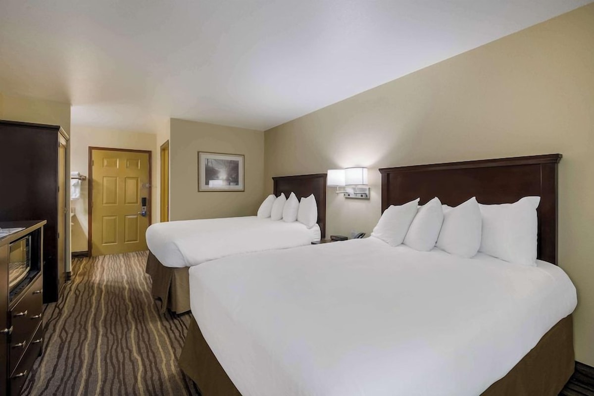 A hotel room with two beds, a television, a desk, and a door.