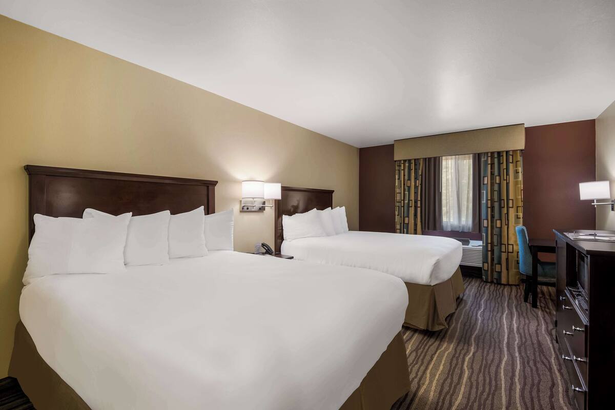 Une chambre d’hôtel avec deux lits, un bureau, une chaise et un téléviseur.