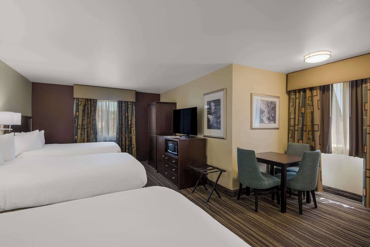 Une chambre d’hôtel avec deux lits, un bureau avec une télévision, une petite table avec des chaises et un tableau encadré au mur.