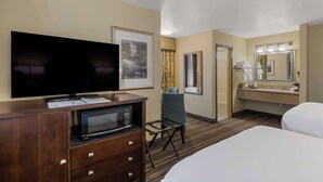 A hotel room with a flat-screen TV, a microwave, a desk with papers, a chair, a bed, a bathroom with a mirror, and a sink. - Best Western Cottage Grove Inn (Cottage Grove)