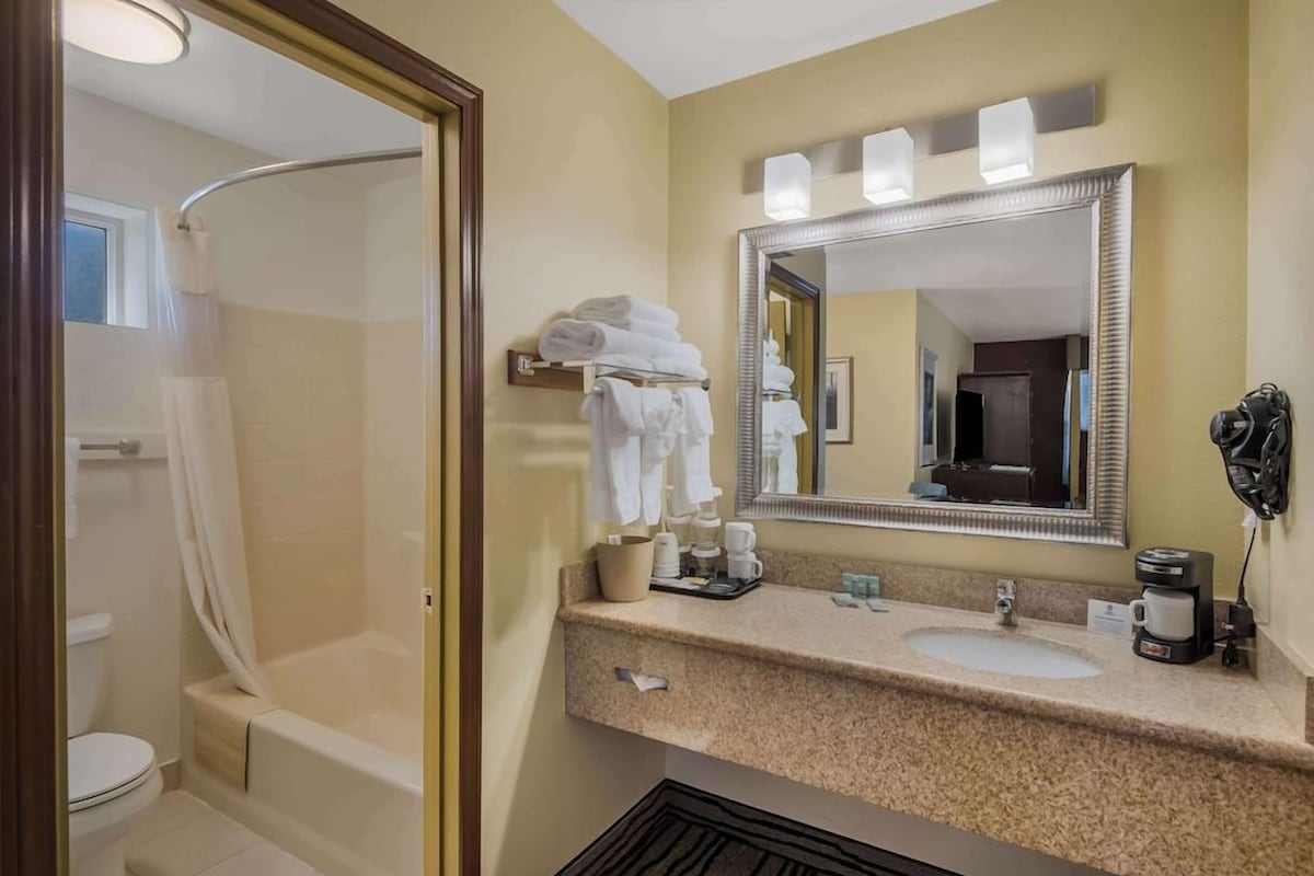 A bathroom with a shower, toilet, and sink. There are towels and toiletries on the sink counter.
