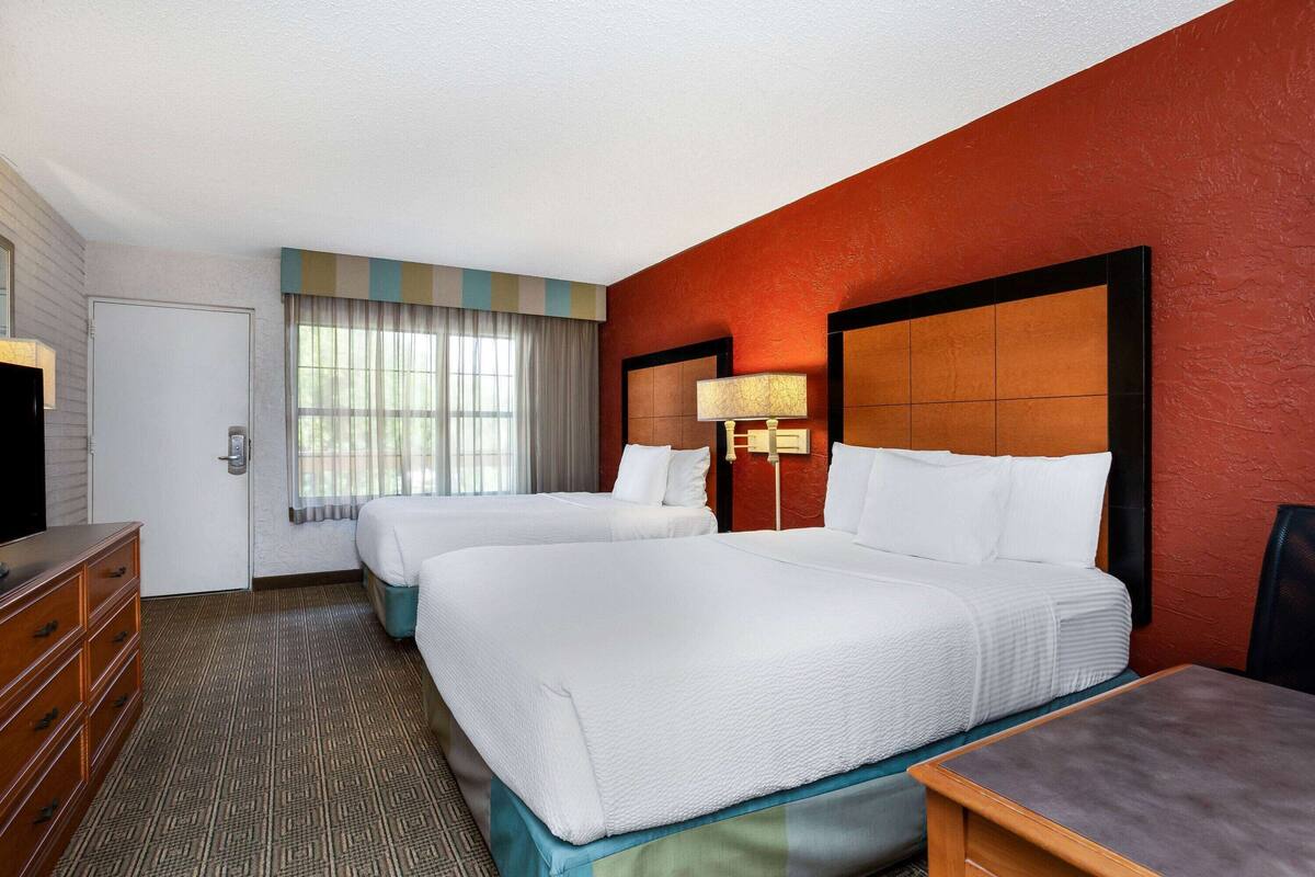 Habitación de hotel con dos camas, un aparador, un televisor y una ventana con cortinas.