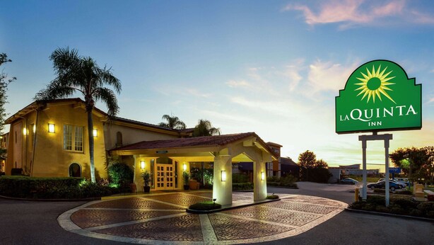 A hotel entrance with a covered waiting area, palm trees, and a sign for La Quinta Inn. - La Quinta Inn Tampa Airport Stadium Westshore (Tampa)